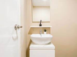 A bathroom with a white sink, a mirror above it, and a small potted plant on the countertop. - Soft Minimalist Studio Room At Meikarta Apartment (Cikarang)