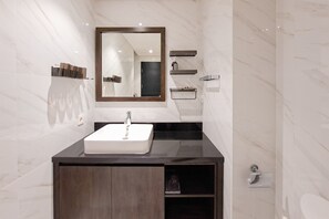 Un baño moderno con pared de mármol, un espejo grande, un lavabo blanco y un mueble de tocador oscuro.