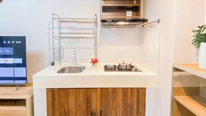 A compact kitchen with a stainless steel sink, a gas stove, and a built-in oven. There is a small shelf above the stove and a wooden cabinet below. - Simple 1Br Near Dian Harapan School At Apartment Meikarta (Cikarang)