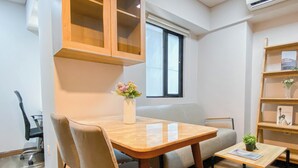 A modern living room with a wooden table, two chairs, a small coffee table, a bookshelf, and a window with blinds. - Simple 1Br Near Dian Harapan School At Apartment Meikarta (Cikarang)