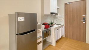 Cocina compacta con un refrigerador de acero inoxidable, un microondas, un lavamanos con un grifo moderno y una puerta de madera.