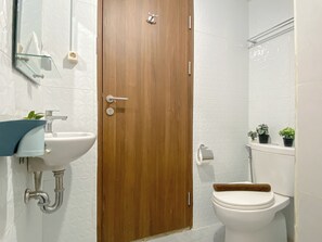 Un baño con puerta de madera, un lavamanos blanco, un inodoro y un espejo.