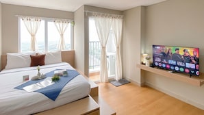 Una habitación de hotel con cama, televisor sobre un soporte y balcón con cortinas.