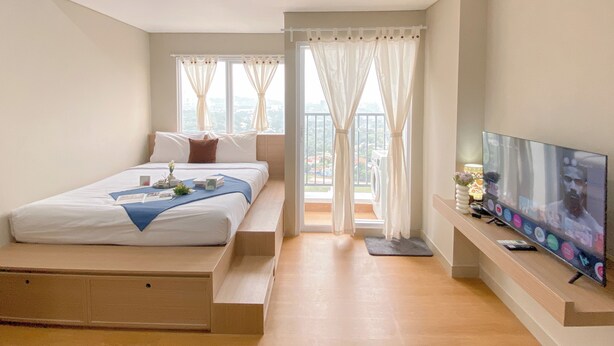 Un dormitorio con cama, televisor, ventana con cortinas y balcón.