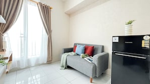 Ein modernes Wohnzimmer mit grauem Sofa, roten und blauen Kissen, einem schwarzen Kühlschrank und einem weißen Fliesenboden.