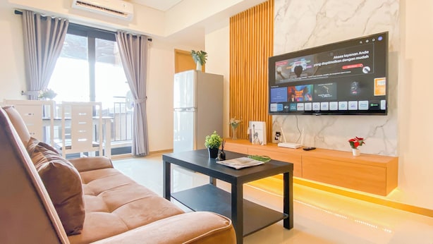 Egy modern nappali, amelyben van egy kanapé, egy dohányasztal, a falra szerelt televízió, és egy kilátással rendelkező erkély.
