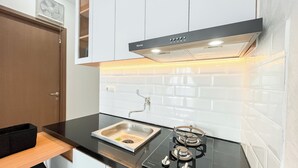 A modern kitchen with a black countertop, white tiled backsplash, a stainless steel sink, and a gas stove. - Minimalist 2Br Apartment At Podomoro Golf View (Gunung Putri)
