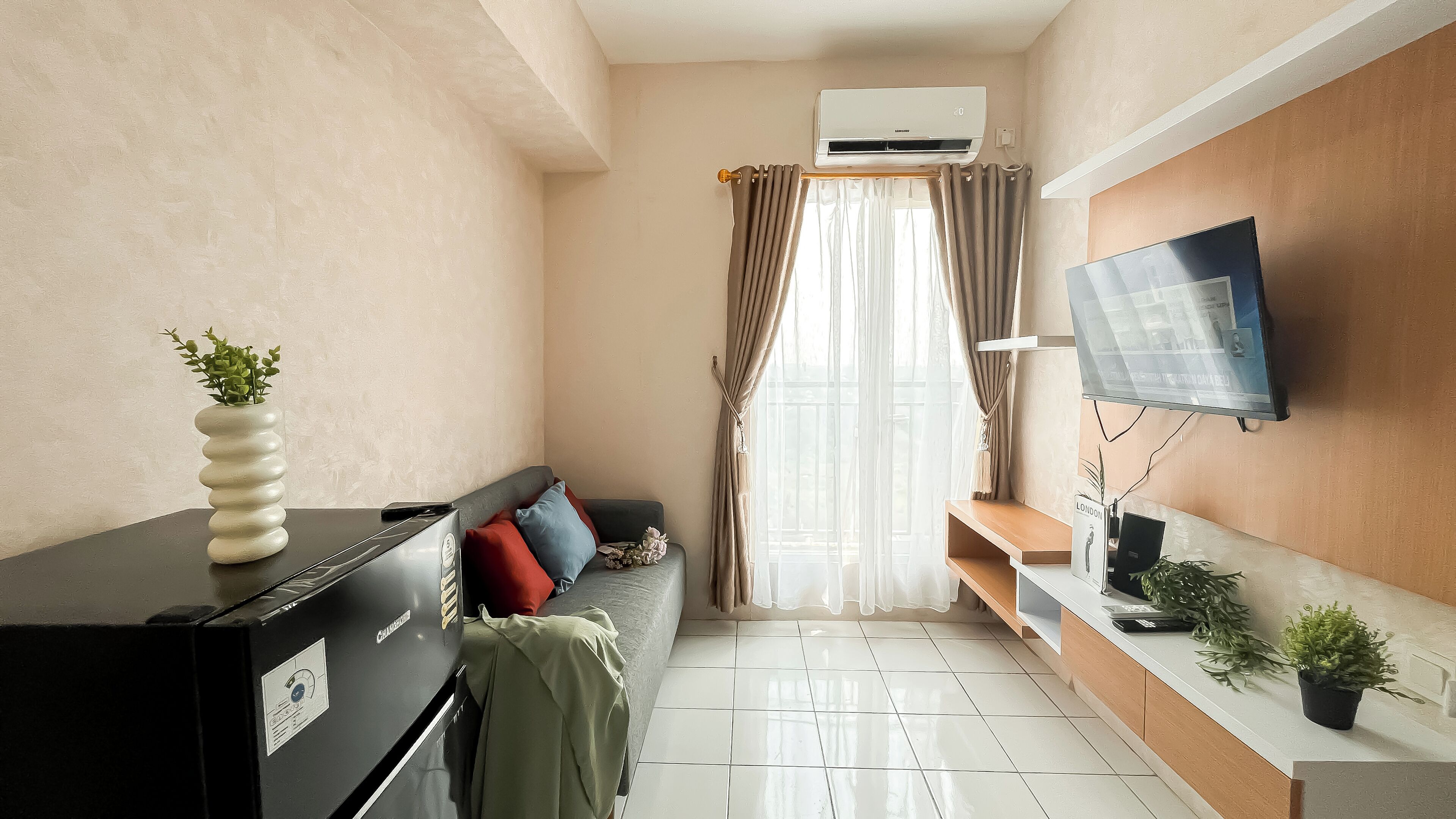 A compact living space with a sofa, a small table, a TV mounted on the wall, and an air conditioning unit.