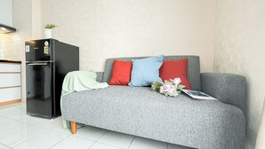 A modern living room with a grey sofa, red and blue cushions, a black refrigerator, and a small plant on top. - Minimalist 2Br Apartment At Podomoro Golf View (Gunung Putri)