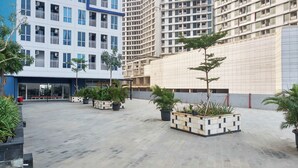 A modern building with multiple floors, outdoor seating area, and potted plants. - Cozy And Modern Style Studio At Grand Dhika City Apartment (Bekasi)