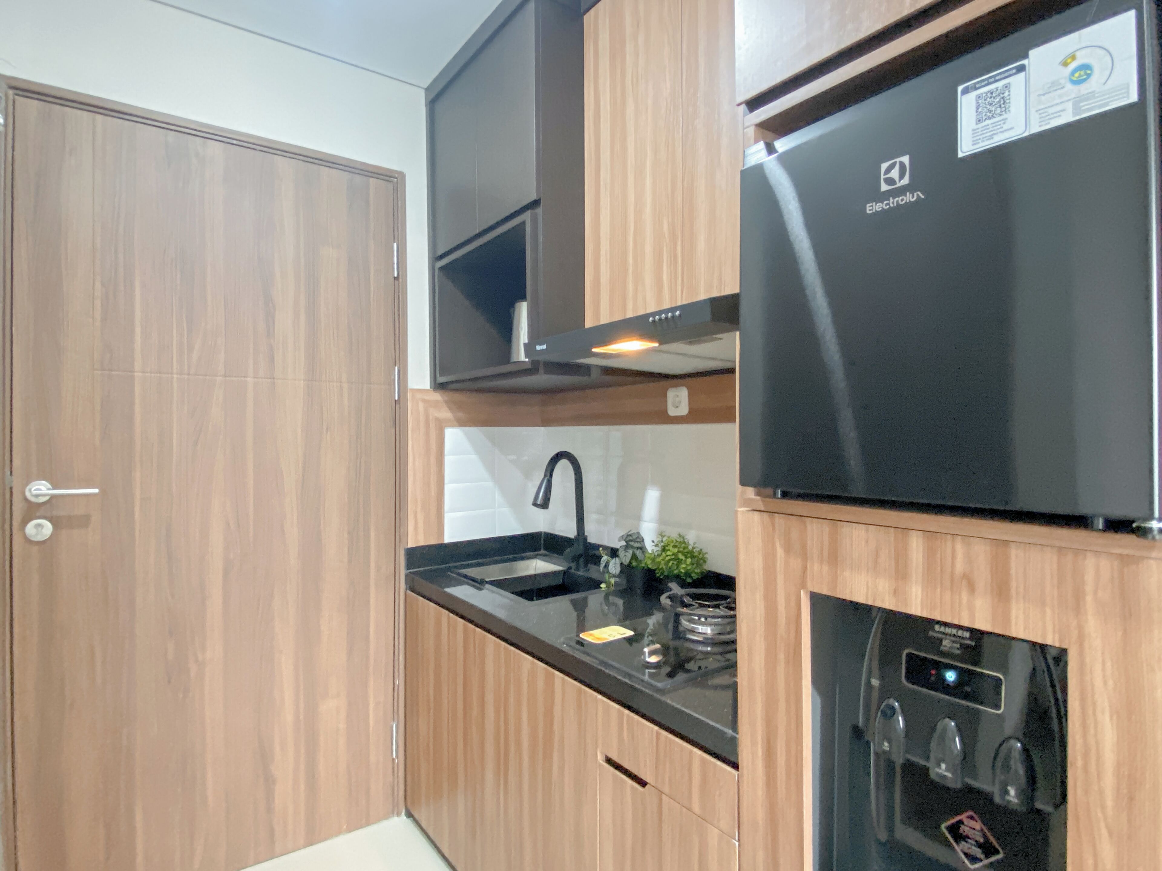 A modern kitchen with wooden cabinets, a stainless steel refrigerator, a built-in oven, and a sink with a faucet.