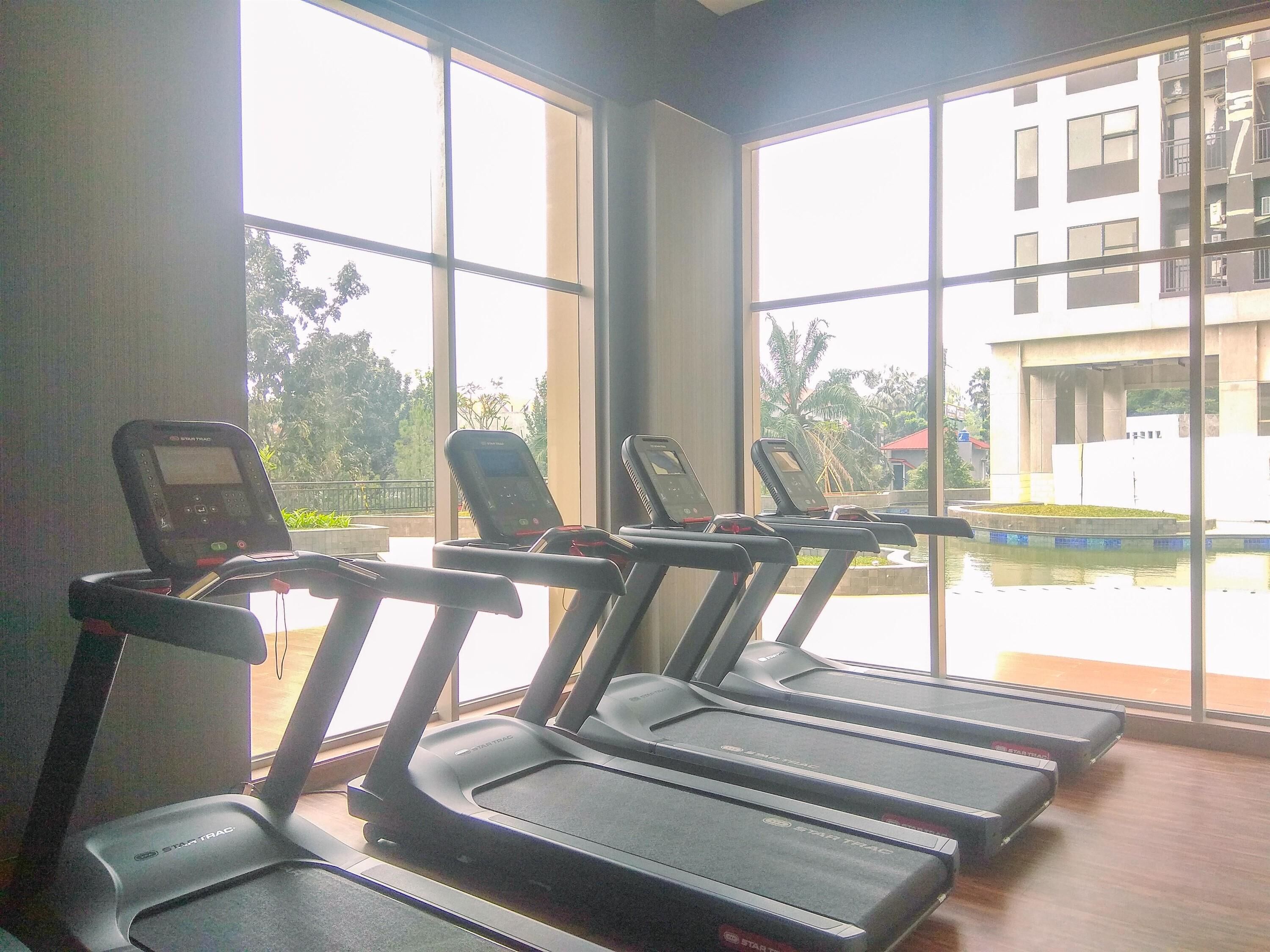 A gym with treadmills, large windows, and a view of a building and trees outside.