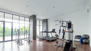 A spacious gym with cardio machines, weightlifting equipment, and large windows offering views of greenery. - Modern 2Br Apartment At Cordova Edupartment Semarang (Semarang)
