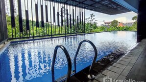 An indoor swimming pool with clear water, metal railings, and a view of greenery and buildings in the background. - Modern 2Br Apartment At Cordova Edupartment Semarang (Semarang)