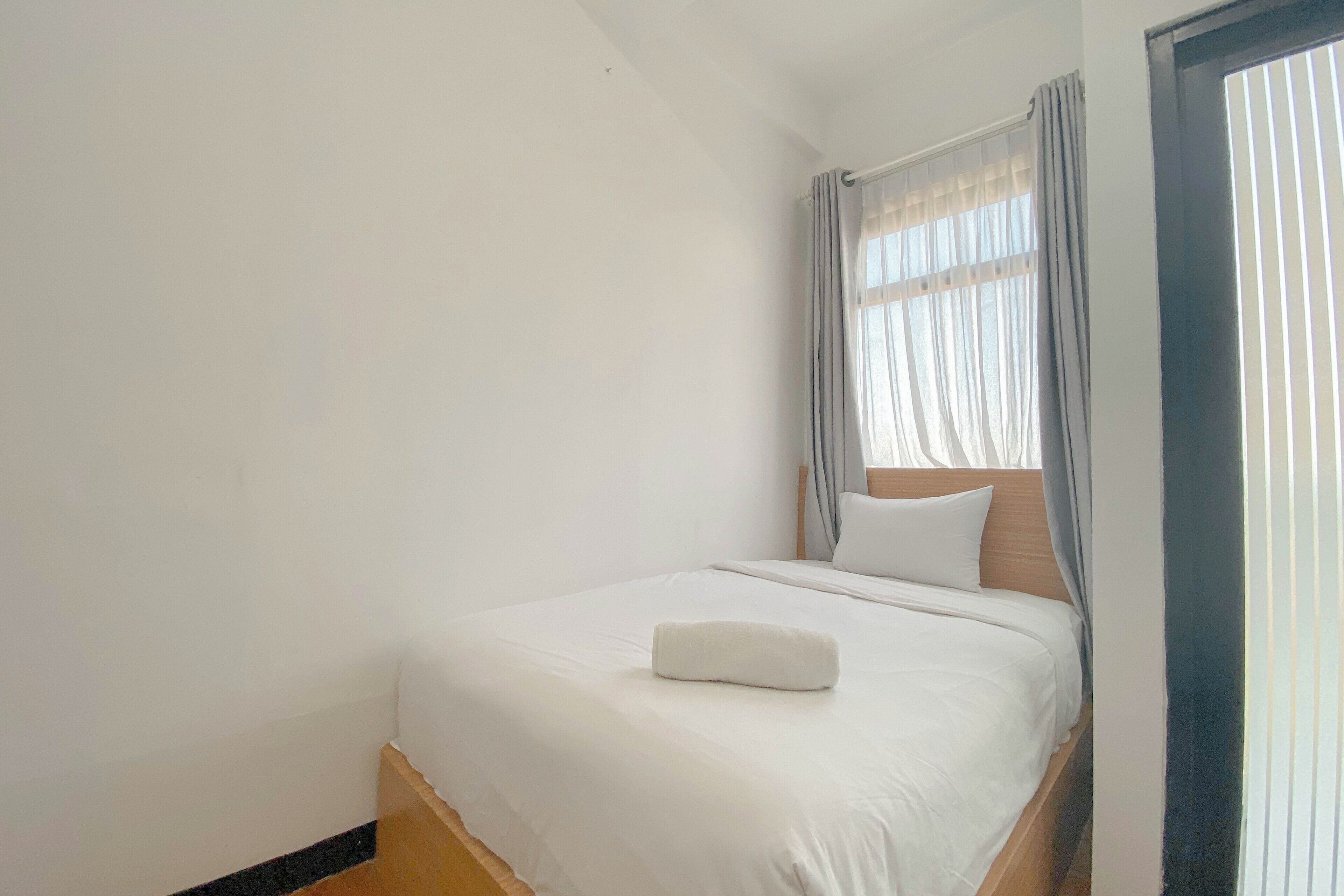A neatly made bed with white bedding and a pillow, a wooden headboard, and a window with curtains.