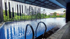 An indoor swimming pool with clear water, metal railings, and a view of greenery and buildings in the background. - Modern 2Br Apartment At Cordova Edupartment Semarang (Semarang)