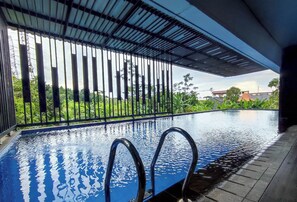 An indoor swimming pool with clear water, metal railings, and a view of greenery and buildings in the background. - Modern 2Br Apartment At Cordova Edupartment Semarang (Semarang)