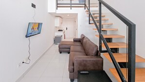 A modern living room with a brown sectional sofa, a black coffee table, and a staircase with wooden steps and black railings.
