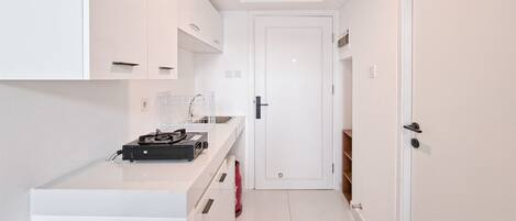 Una cocina moderna y estrecha con armarios blancos, una encimera con una cafetera y una puerta que da a otra habitación.