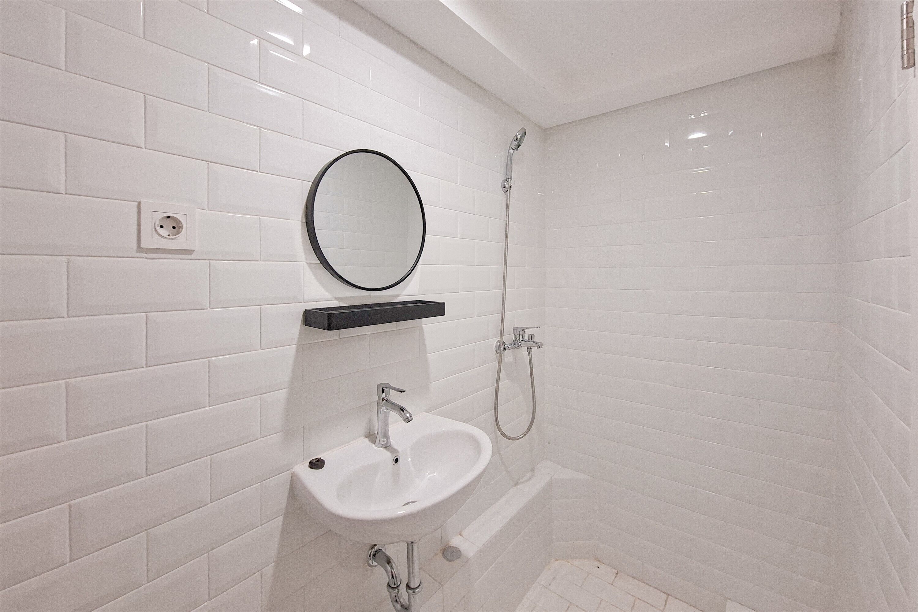 Un baño con paredes de azulejos blancos, un lavamanos blanco, un espejo redondo y una ducha.