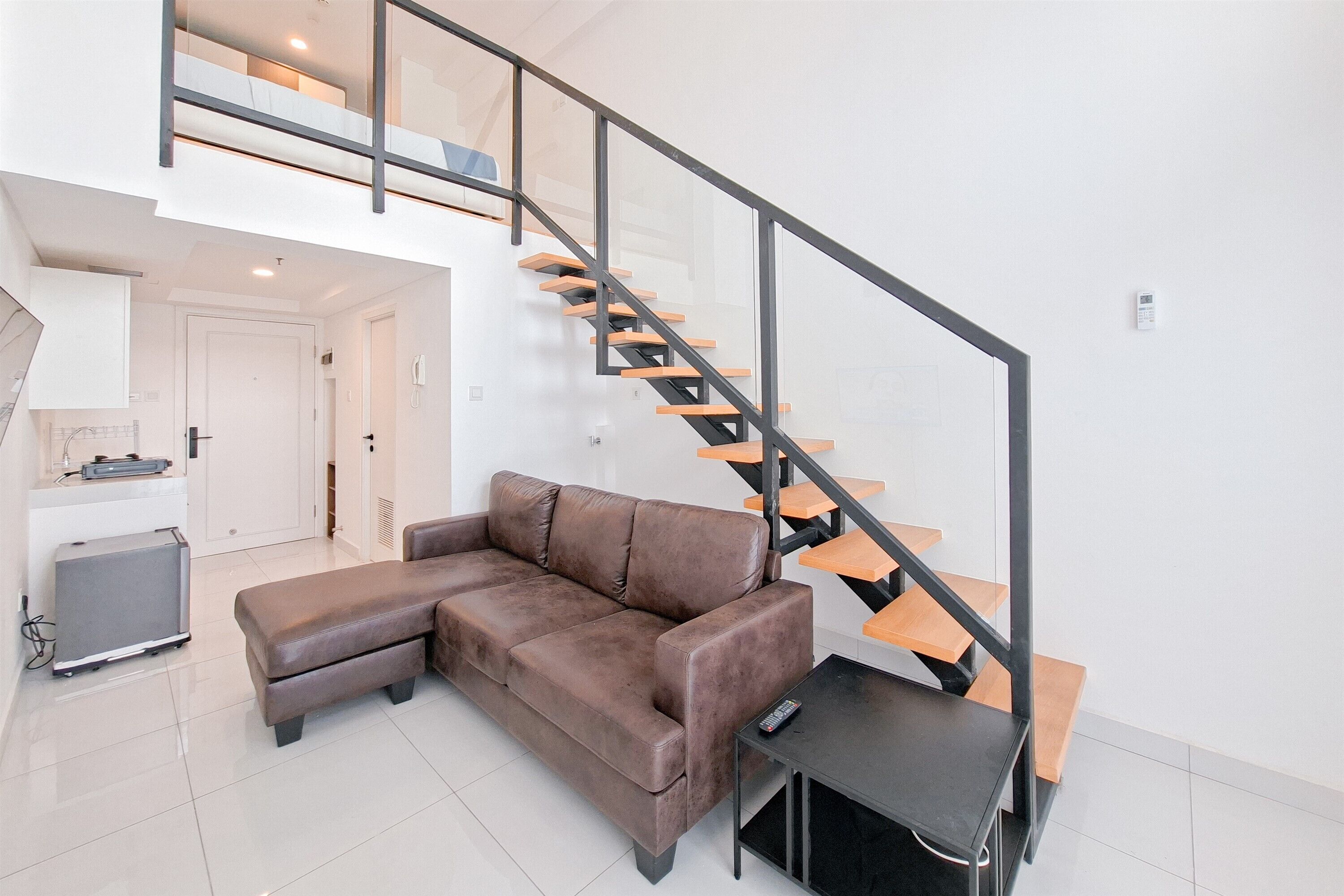 A modern living room with a brown leather sofa, a black coffee table, and a wooden staircase with glass railings.