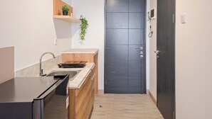 A compact kitchen with a dark door, a wooden countertop, a sink, and a small shelf with a plant.