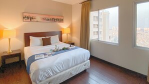 A hotel room with a large bed, two bedside lamps, a city view, and a painting on the wall. - Good Deal 1Br Apartment At Marina Ancol (Jakarta)