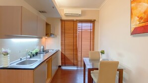 A compact kitchen with a sink, stove, and cabinets, leading to a dining area with a table and chairs. - Good Deal 1Br Apartment At Marina Ancol (Jakarta)