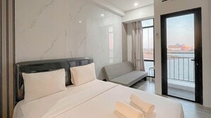 A hotel room with a large bed, a sofa, a balcony with a view of the water, and marble walls. - Modern Scandinavian Studio At Delft Ciputra Makassar Apartment (Makassar)