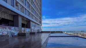 A rooftop pool area with a view of the sea, a modern building with multiple floors, and a clear sky. - Modern Scandinavian Studio At Delft Ciputra Makassar Apartment (Makassar)
