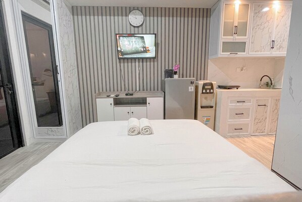 Habitación de hotel con cama, televisión montada en la pared, kitchenette pequeña y baño con ducha.