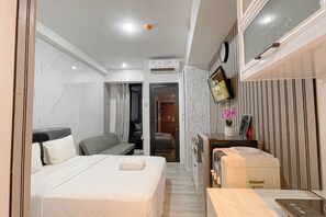 Habitación de hotel con cama, escritorio, silla, aire acondicionado, televisor y espejo.