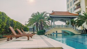 A pool area with lounge chairs, a gazebo, and a bridge over the pool. - Homey 2Br Apartment At Lucky Tower Residence (Jakarta)