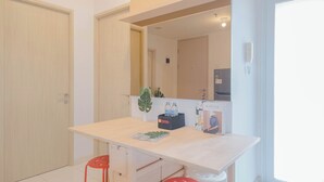 A modern, well-lit room with a wooden desk, two red stools, a mirror, a potted plant, and a Kinturk poster. - 2Br Near Shopping Hub At Tokyo Riverside Pik 2 Apartment (Teluknaga)