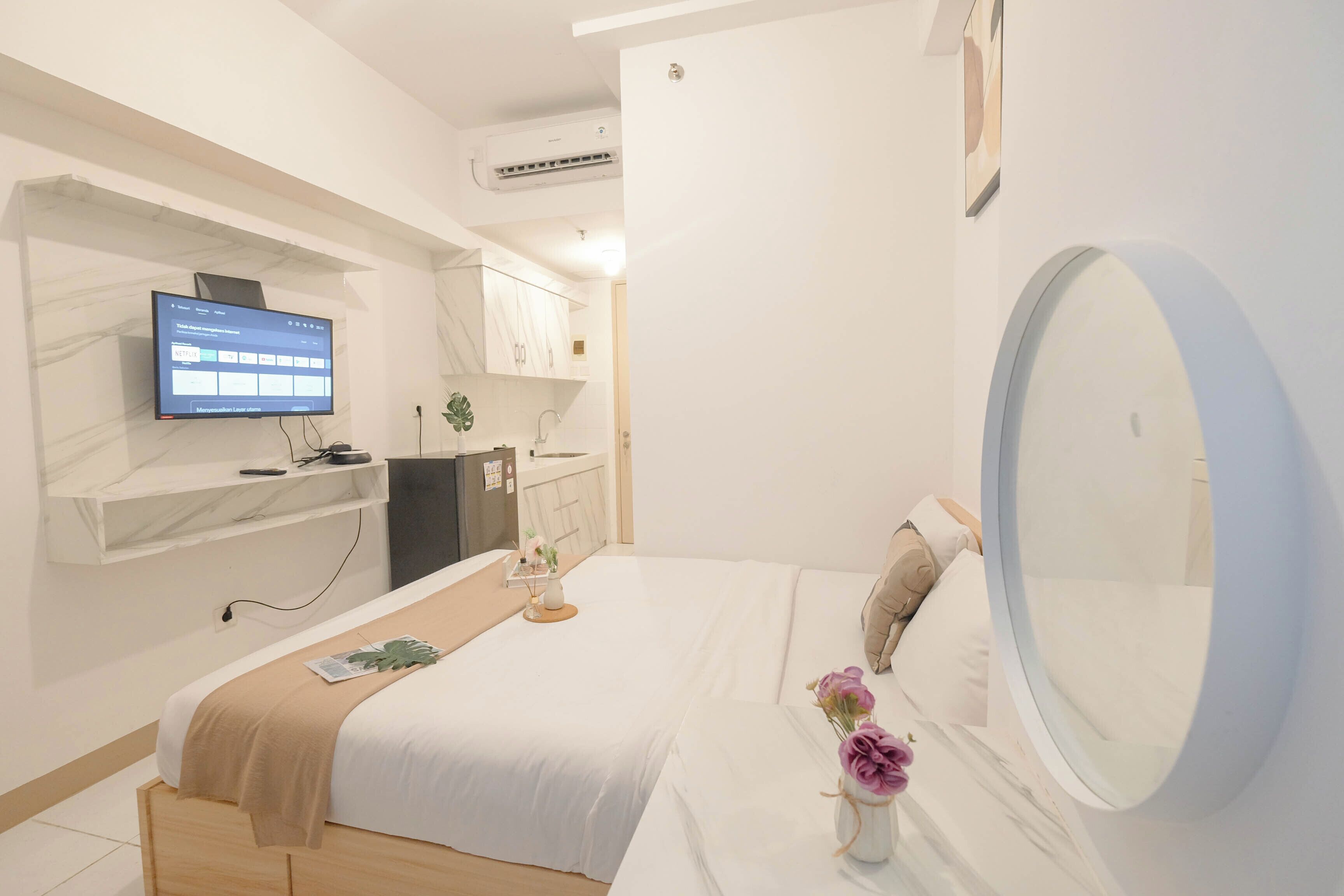 Ein modernes Hotelzimmer mit Bett, Wandfernseher, kleinem Schreibtisch und einem durchgegangenen Tür erkennbaren Badezimmer.