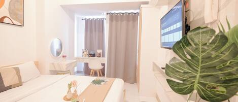 Ein Hotelzimmer mit Bett, Schreibtisch, Fernseher und einer großen Pflanze.