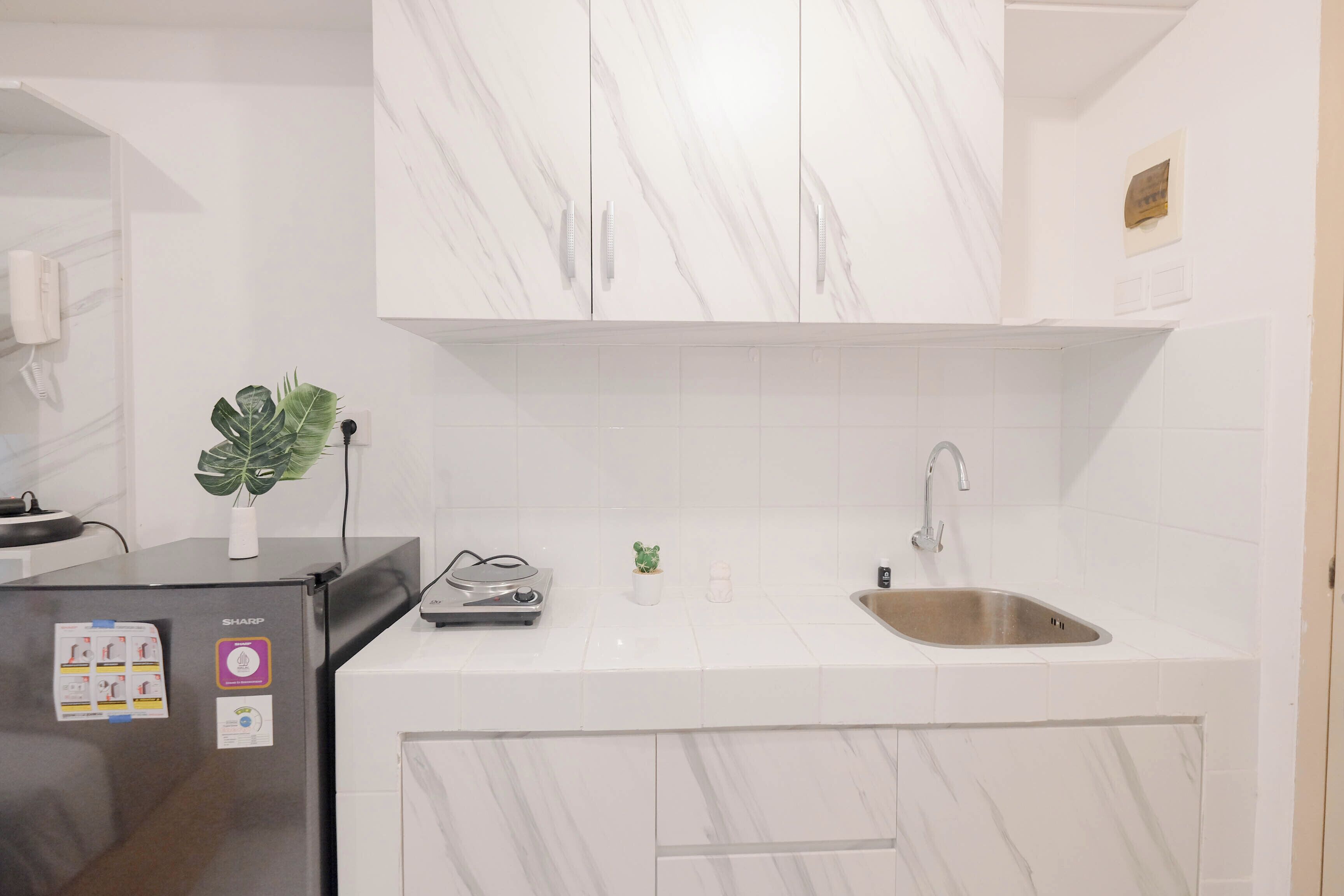 A modern kitchen with white marble tiles, a stainless steel refrigerator, a sink, and a small potted plant.