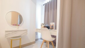 Un baño con tocador blanco, espejo redondo, taburete pequeño, silla blanca y ventana con cortina.