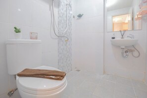 A bathroom with a toilet, shower, sink, and a small potted plant on the toilet.