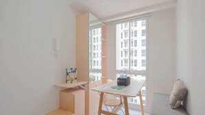 Een moderne, minimalistische kamer met een houten bureau, een bankje en een groot raam met uitzicht op een gebouw.
