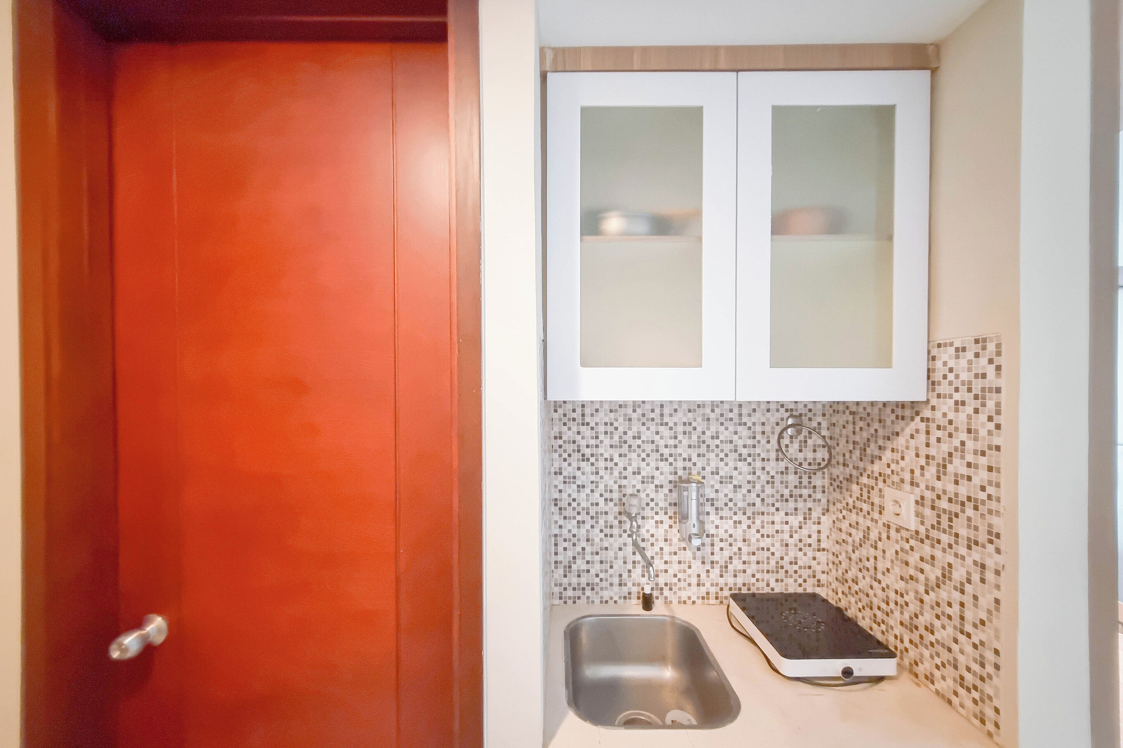 Una cocina pequeña con una puerta roja, un lavamanos y un microondas.