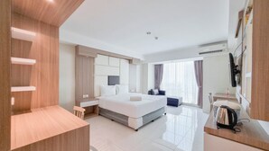 A modern hotel room with a large bed, bedside tables, a desk, and a chair. - Tidy Studio At Mataram City Apartment (Ngaglik)
