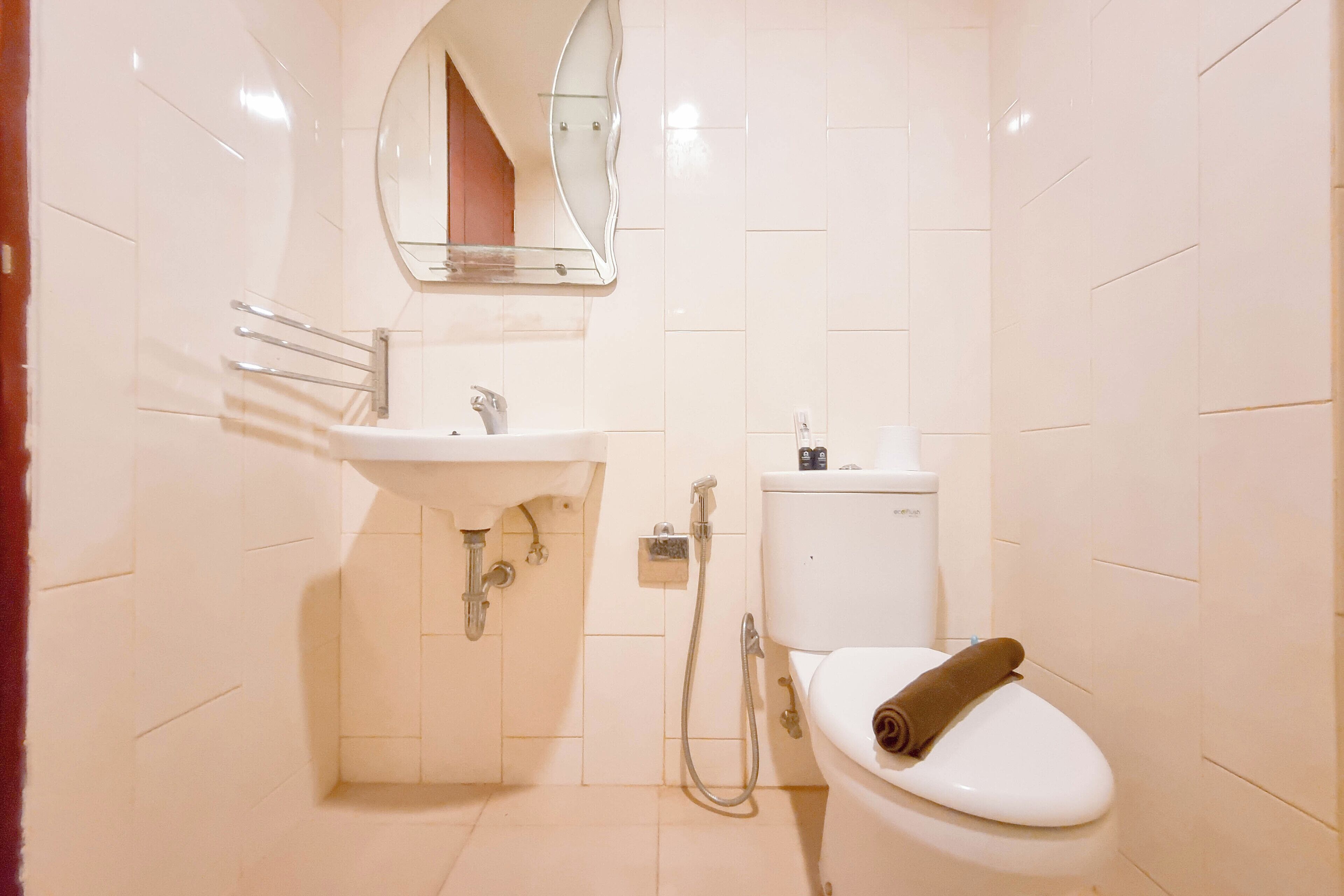 Et lille, rent badeværelse med hvid vask, spejl, toilet og brusebad.