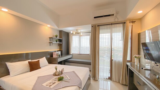 A modern hotel room with a large bed, bedside tables, a TV, and a view of the city through the window. - Best Studio Apartment At Gateway Park Lrt City Jatibening (Bekasi)