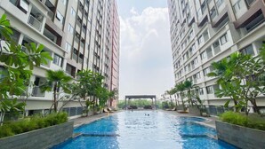 A swimming pool surrounded by high-rise residential buildings with balconies, trees, and a covered area in the center. - Best Studio Apartment At Gateway Park Lrt City Jatibening (Bekasi)