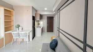 Eine moderne Küche mit weißen Schränken, ein Essbereich mit zwei weißen Stühlen und ein graues Sofa mit einem blauen Kissen.