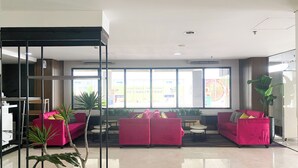 Una hall moderna con illuminazione brillante, un'area salotto con divani rosa e un'ampia vetrata con pubblicità.