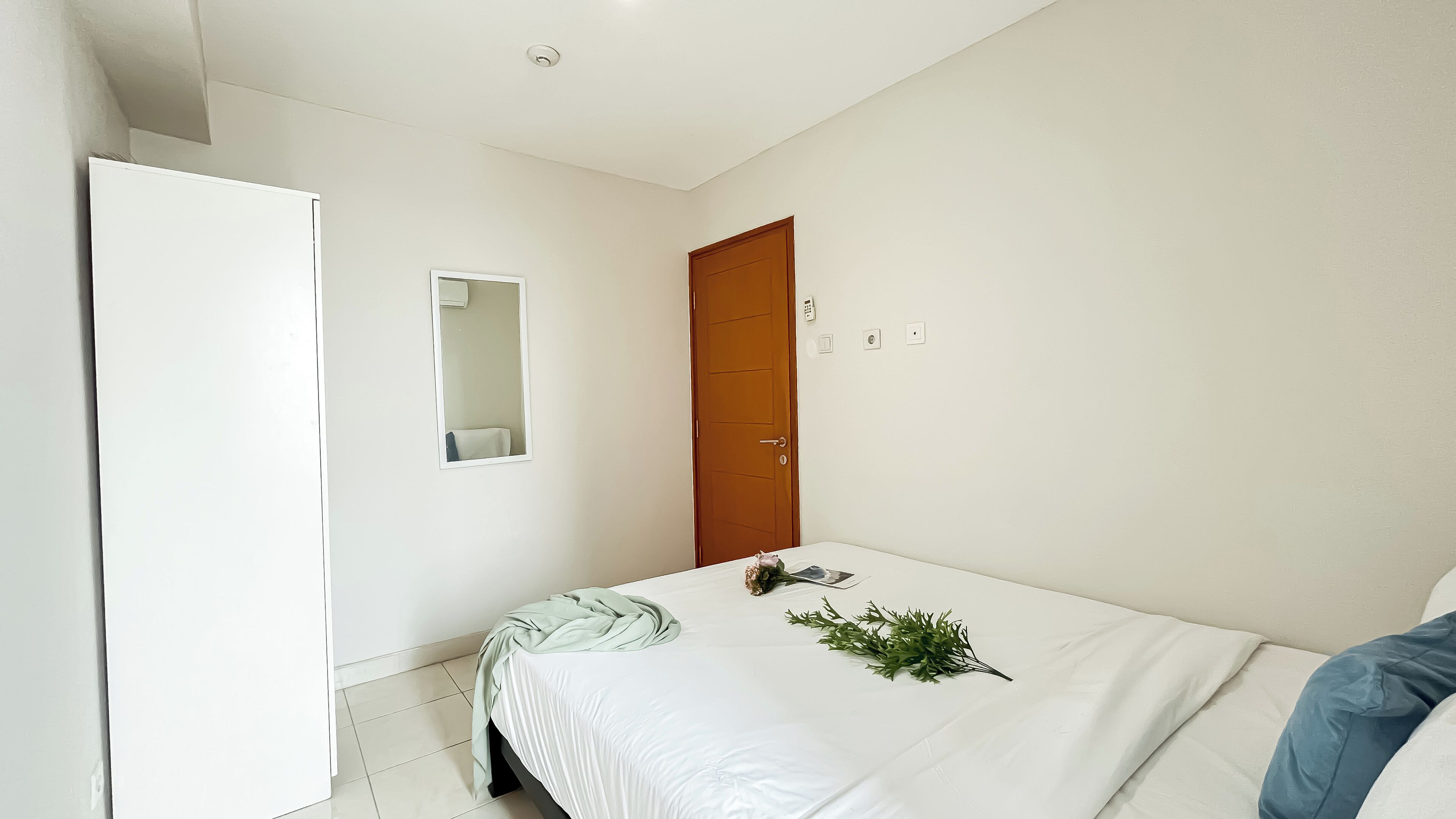 A bedroom with a bed, a wooden door, a white wardrobe, and a mirror on the wall.