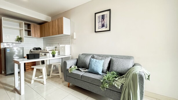 Een moderne keuken met witte kasten, een inbouwkoelkast en een zithoek met een grijze bank en witte stoelen.