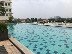 A rooftop swimming pool with a tiled pattern, surrounded by greenery and a view of distant buildings. - Scandinavian Minimalist 2Br At Cinere Bellevue Suites Apartment (Depok)